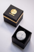Black box with a gold emblem containing a white marble-textured round object on a light gray background